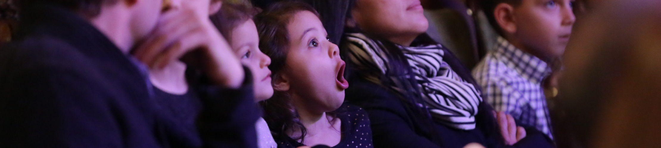 Audience members enjoy a live performance, including one young girl who watches with her mouth agape