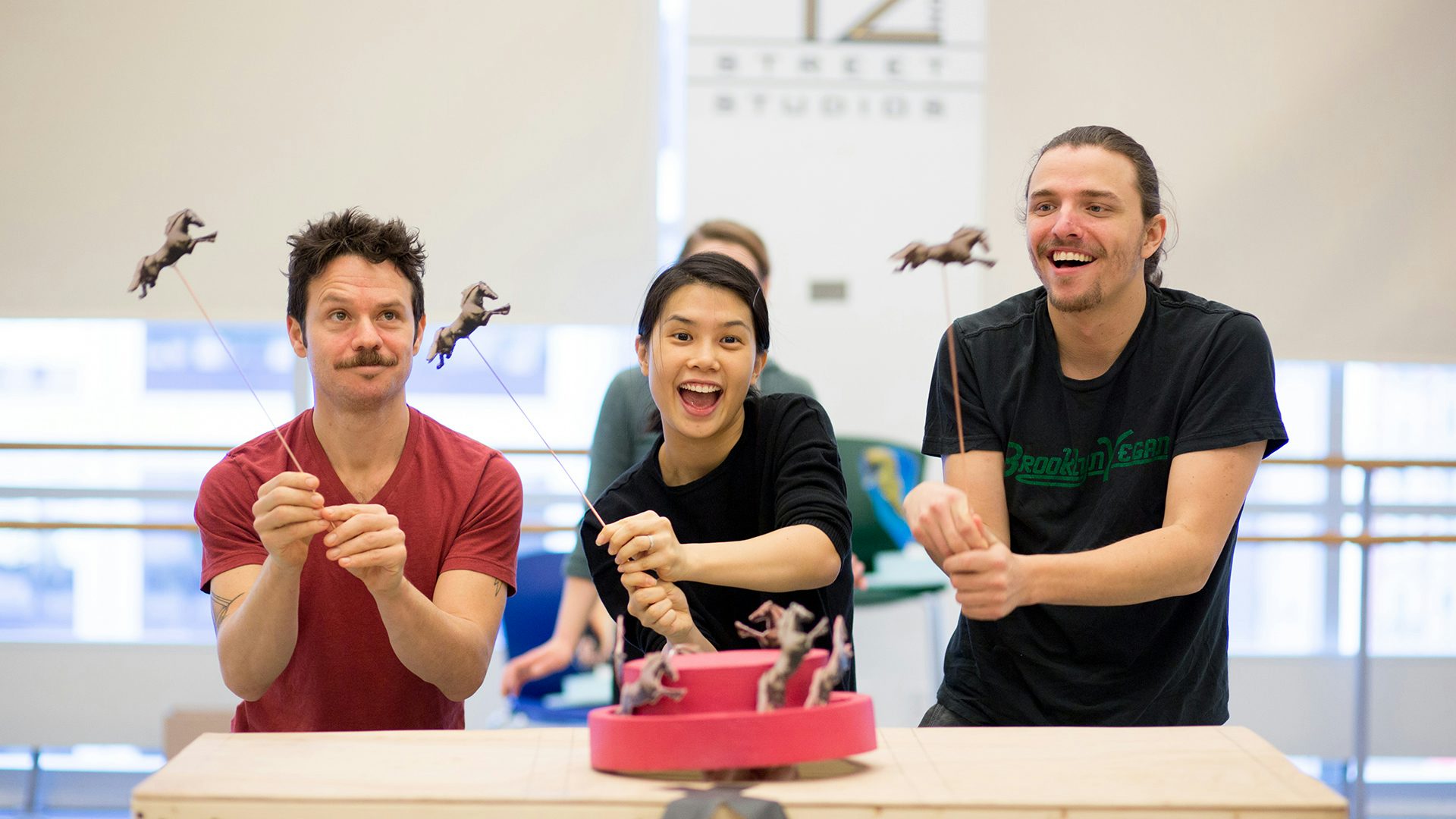 Three actors operate toy horse rod puppets in a rehearsal
