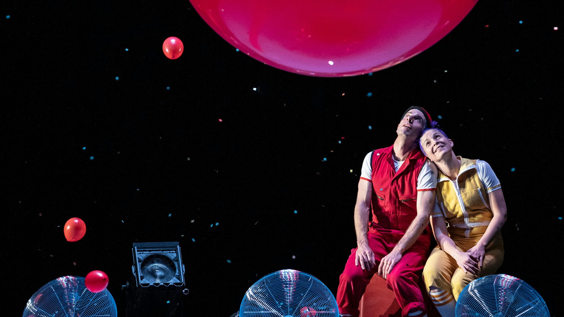 Acrobuffos gazing up in wonder at a giant red floating balloon.