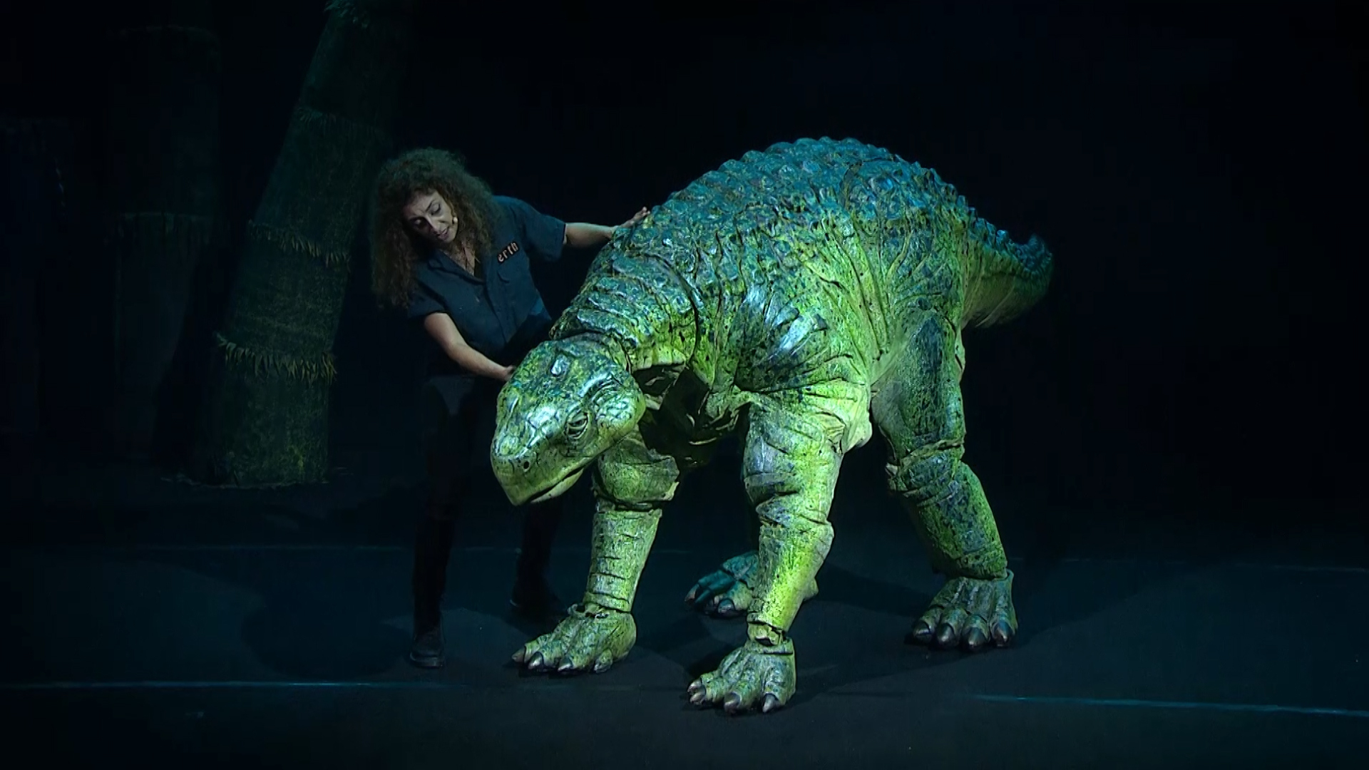 Randa, the show's host, stands next to a life-size puppet of a Minmi Paravertebra dinosaur.