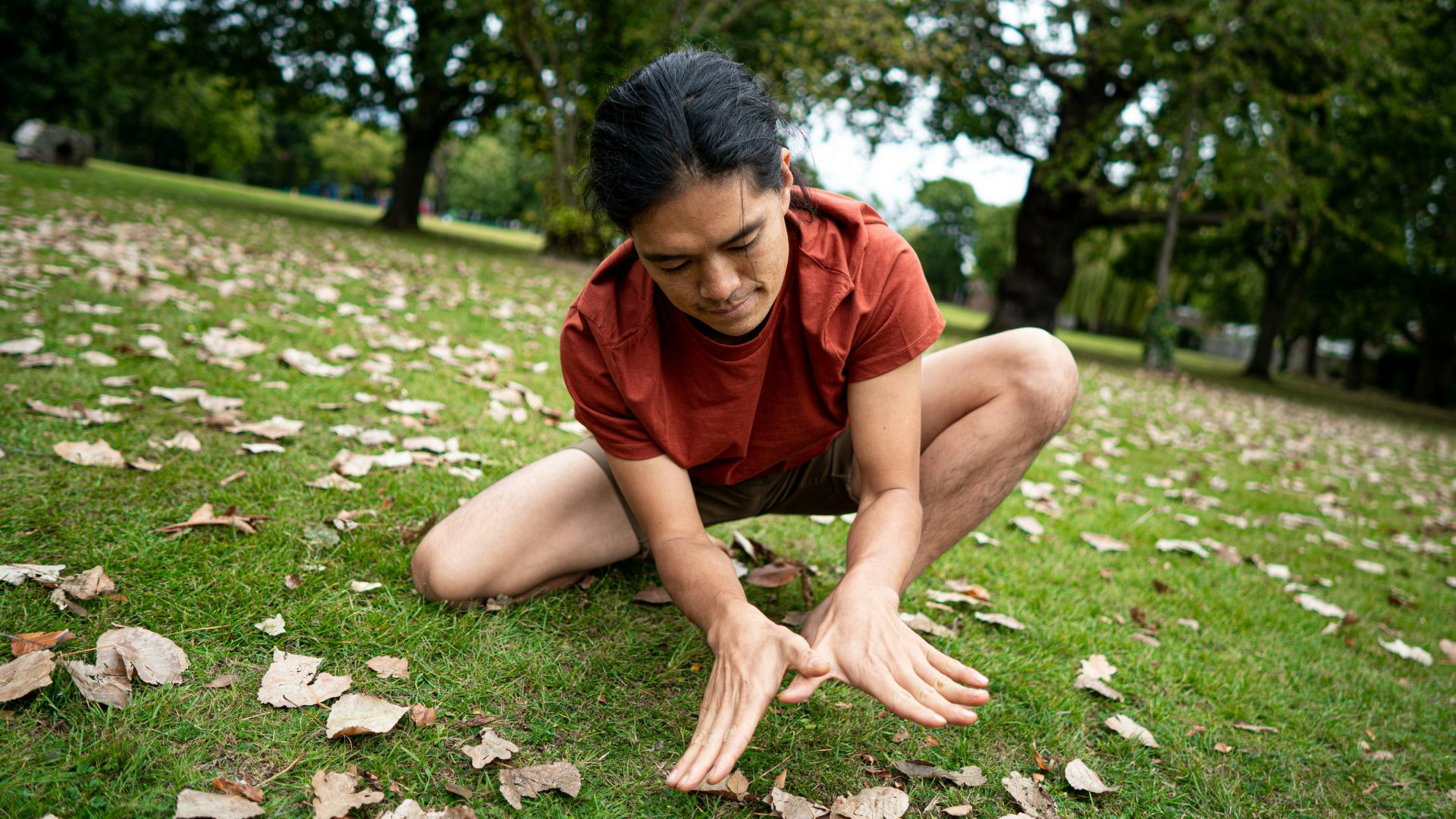 A man, crouched down on the grass, puts his hands together in the shape of a butterfly.