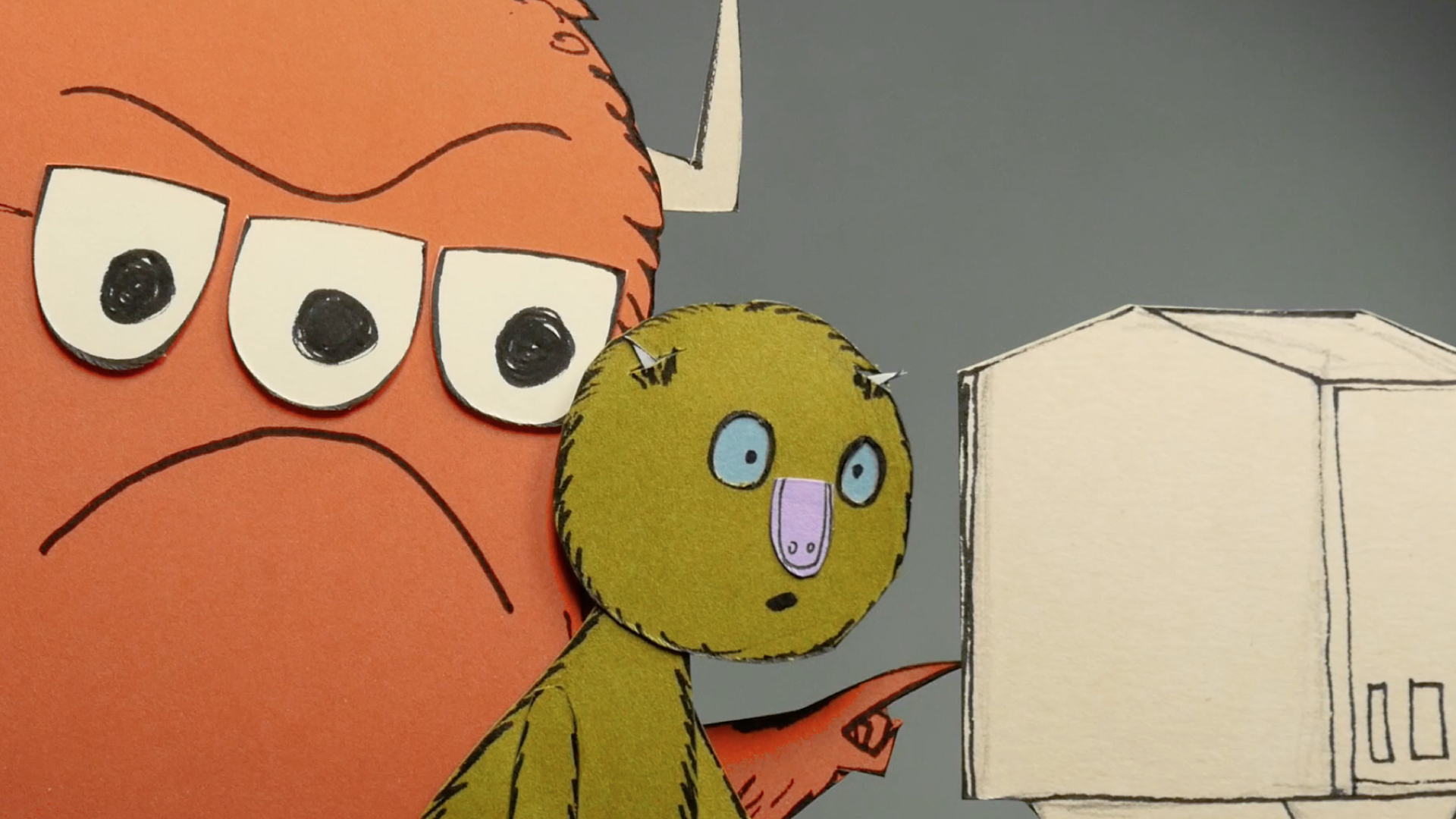 A frowny, three-eyed monster puppet, made from paper, shows Leonardo, also made from paper, information on a computer screen.