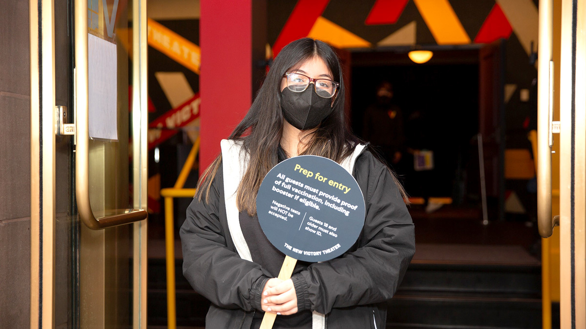 An usher in a mask holds a sign with details on Covid-19 entry requirements.