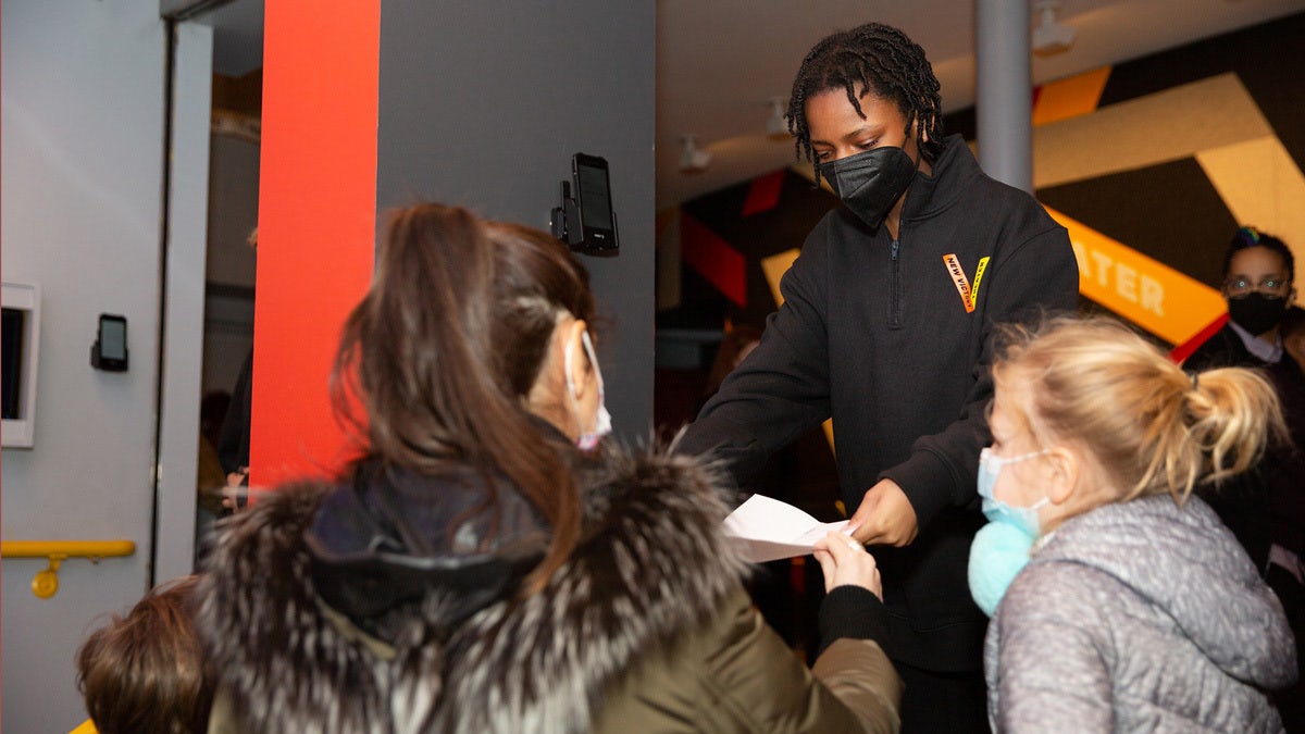 A masked New Victory usher scans a mom and daughter's tickets.