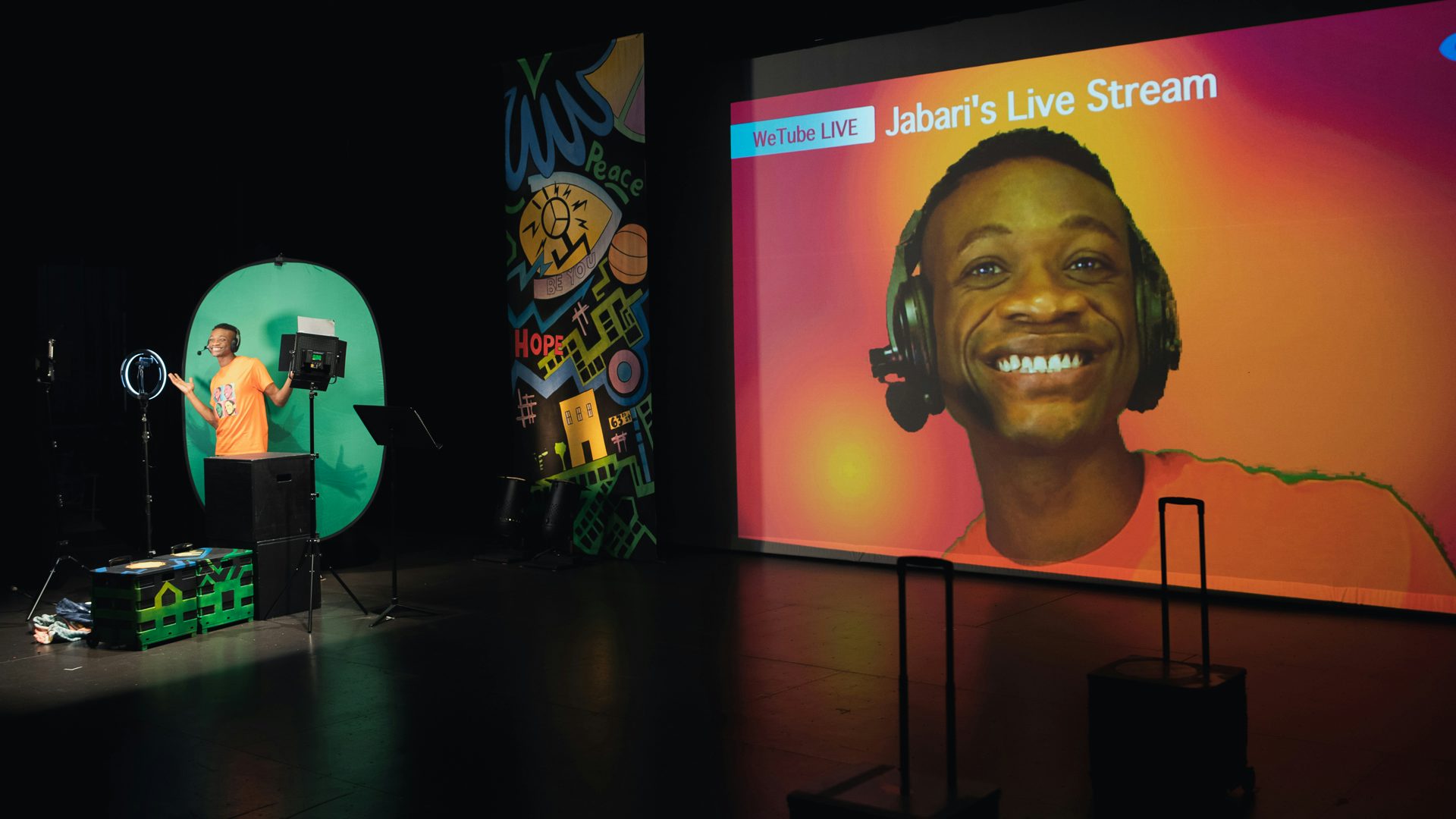 Jabari livestreams in front of a green screen. Beside him, a projection, of the livestream.