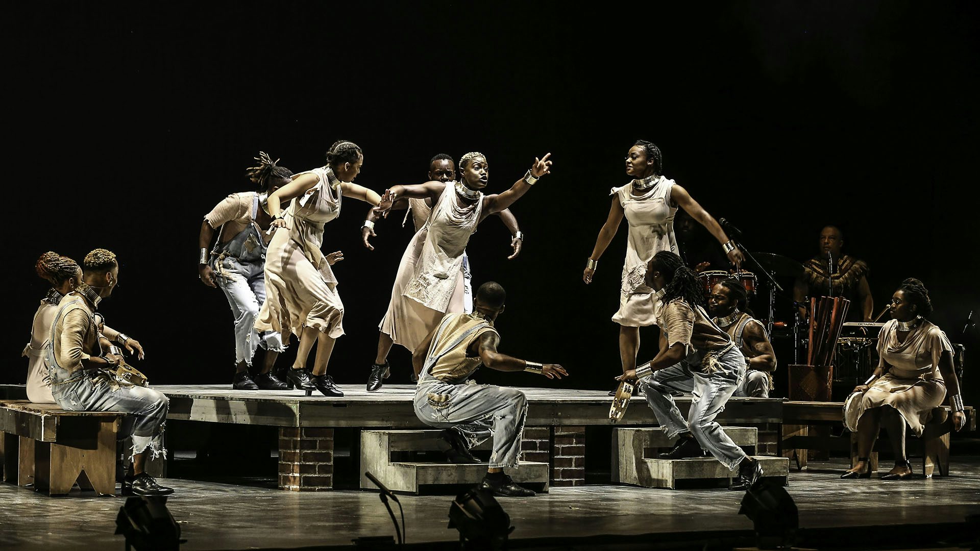A group of Step Afrika's dancers gathered around the stage, with a woman at center.