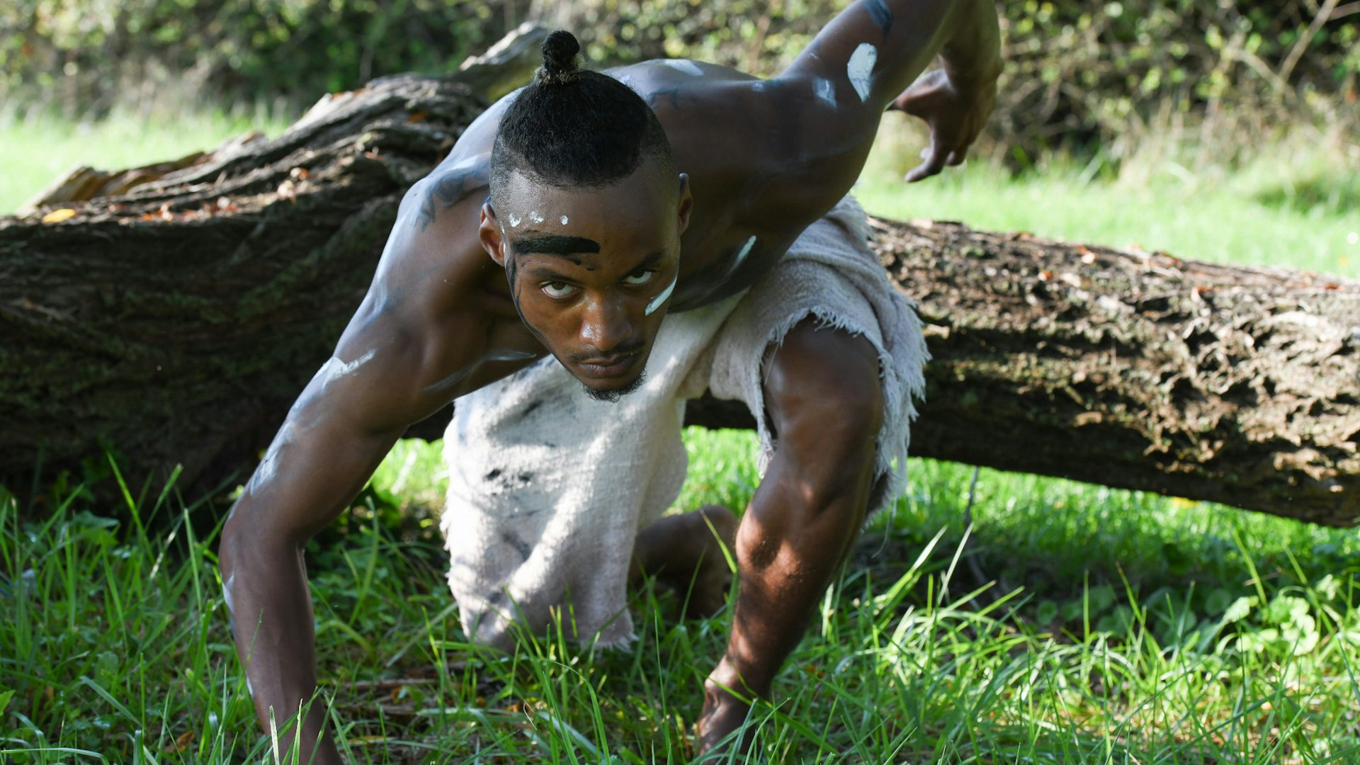 Closeup of a male dancer with African tribal face paint, crouching on one knee,