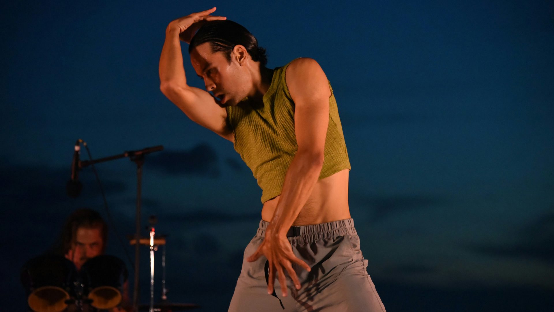 A dancer stands with his arms stretching across his body.