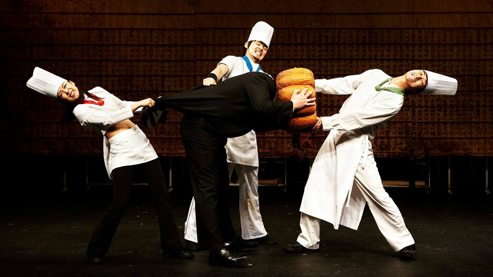 Three chefs try to pull a pumpkin off a man's head.