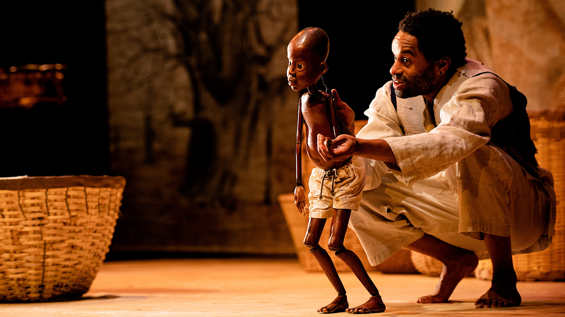 A crouching man operates a puppet of a small boy.