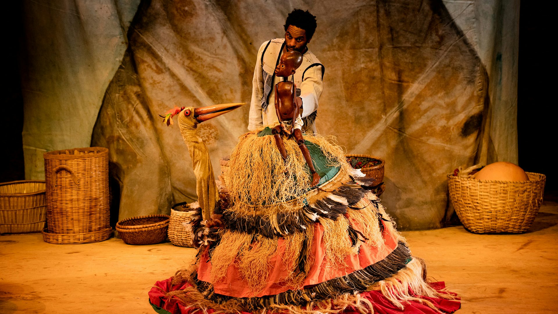 A man operates a puppet of a boy, who is sitting on a crane puppet.