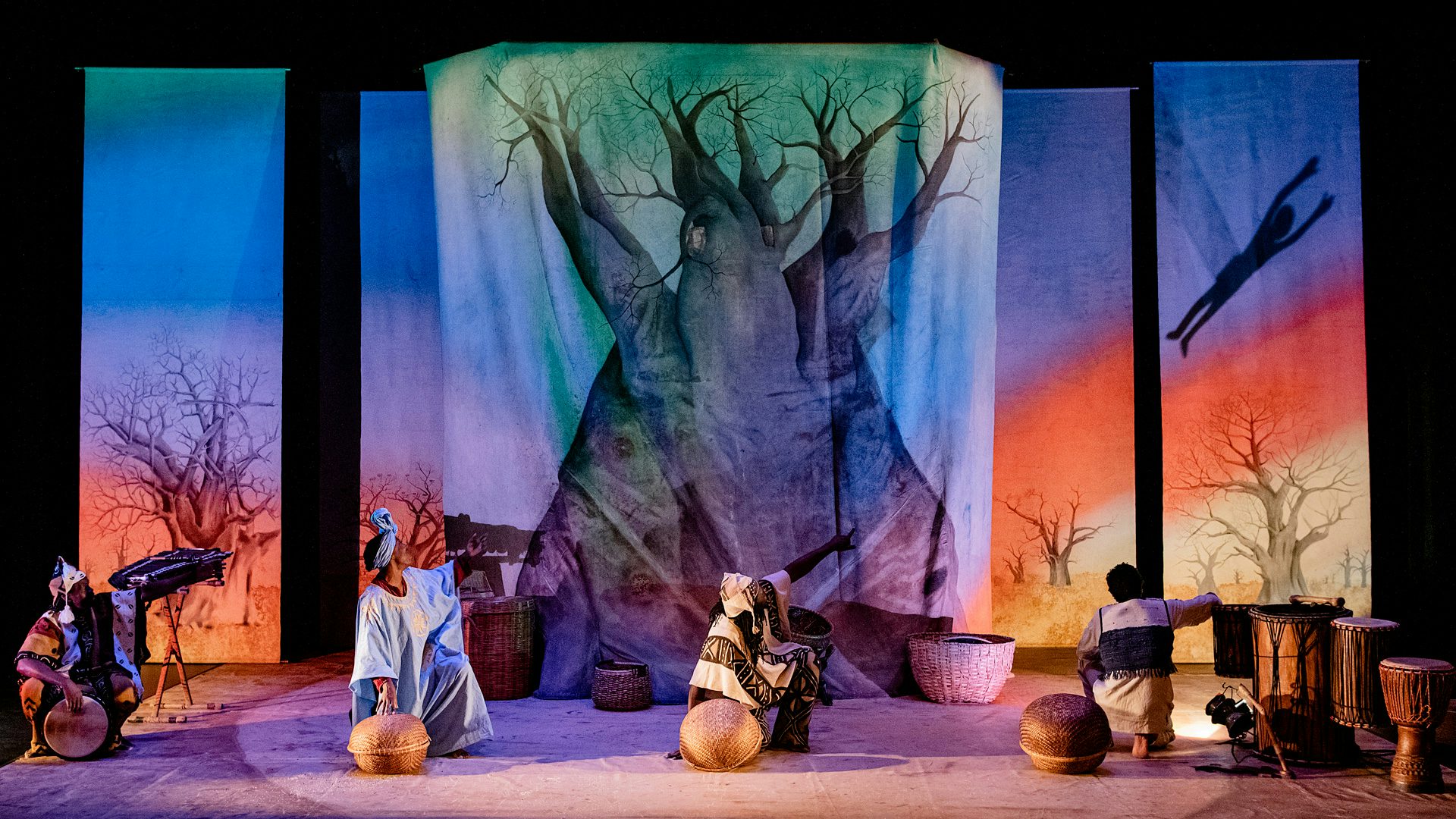 Four actors point at a shadow puppet of a boy flying through a rainbow.