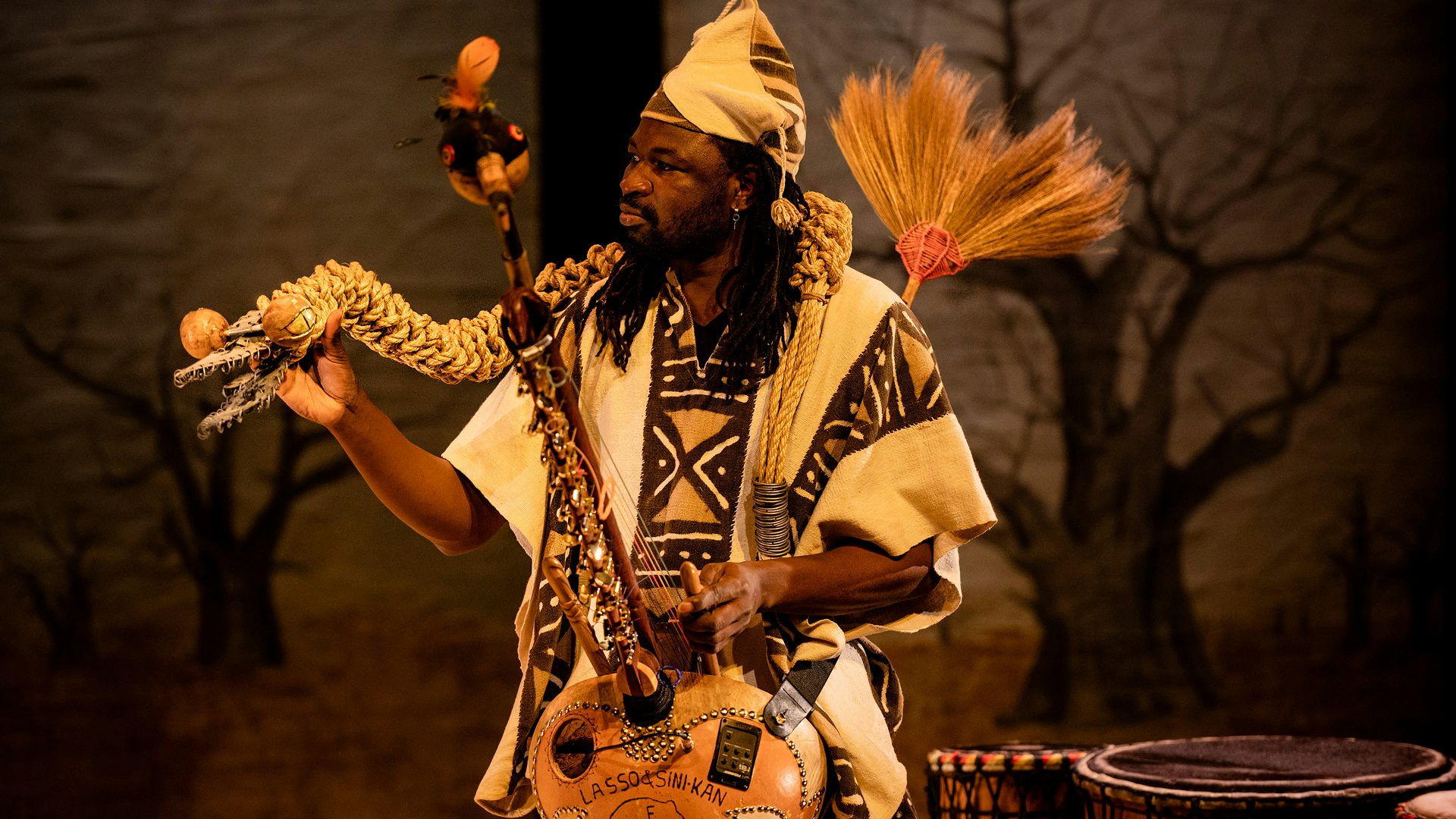 A n'goni player holds a snake puppet made from rope in his hand.