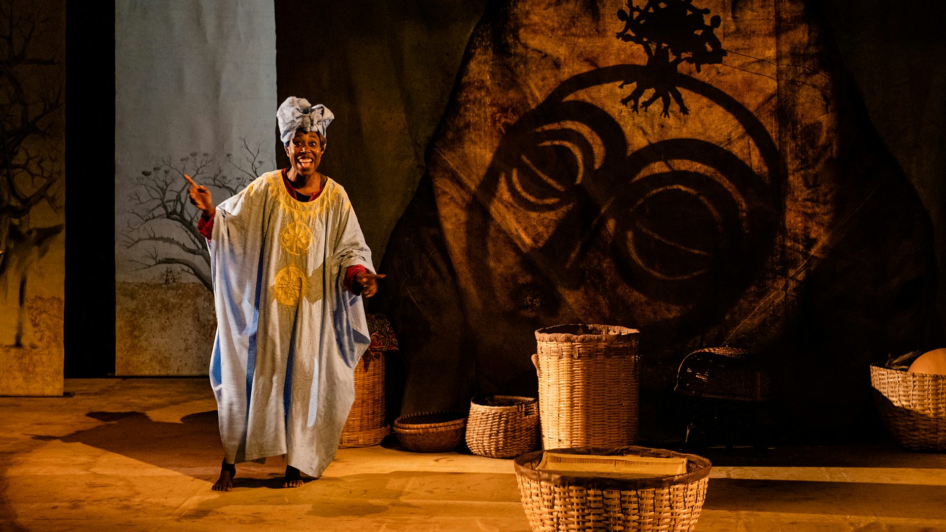 A woman wearing an headwrap and Tunic stands onstage, telling a story.
