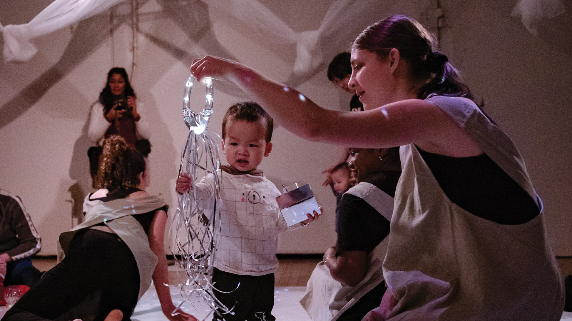 A performer holds a ring of lights, a child reaches out to explore.