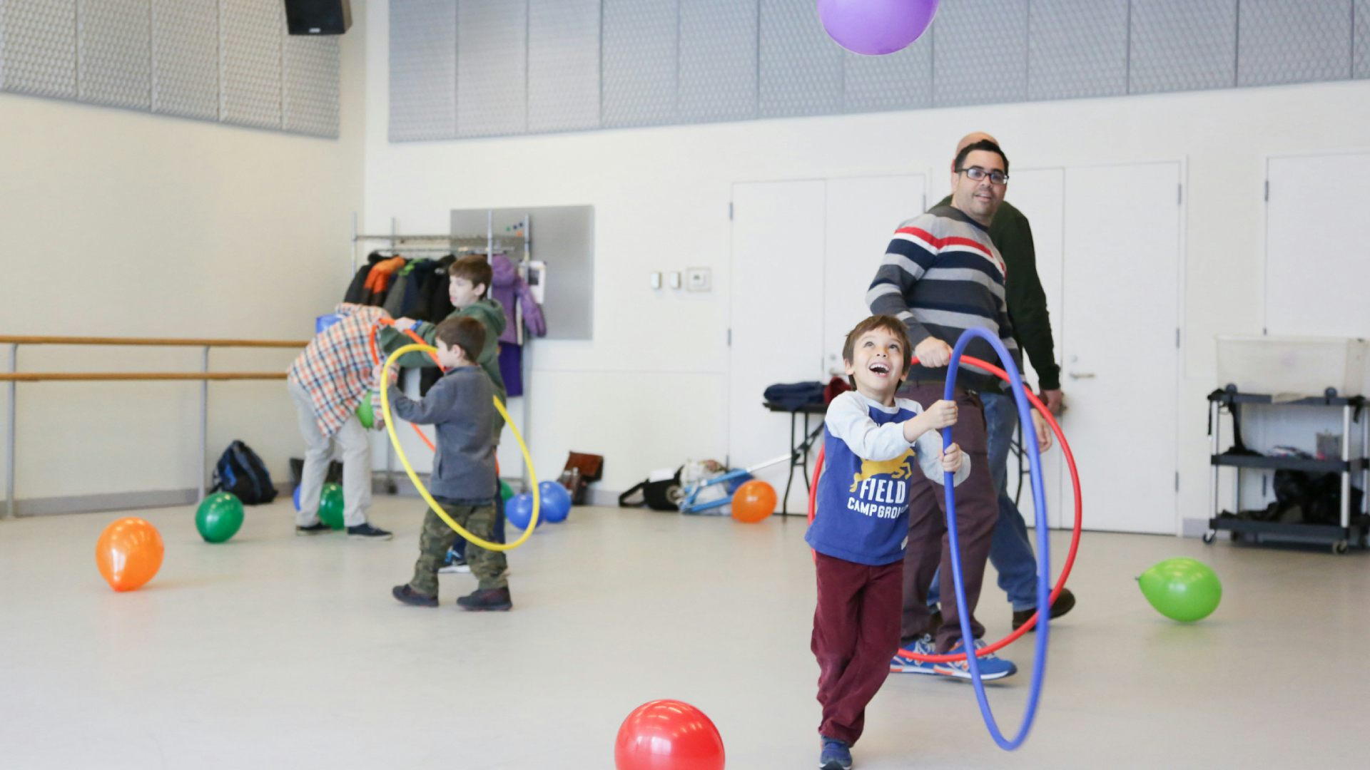 A boy plays with a hula hoop inside a dance studio, with others play behind him.