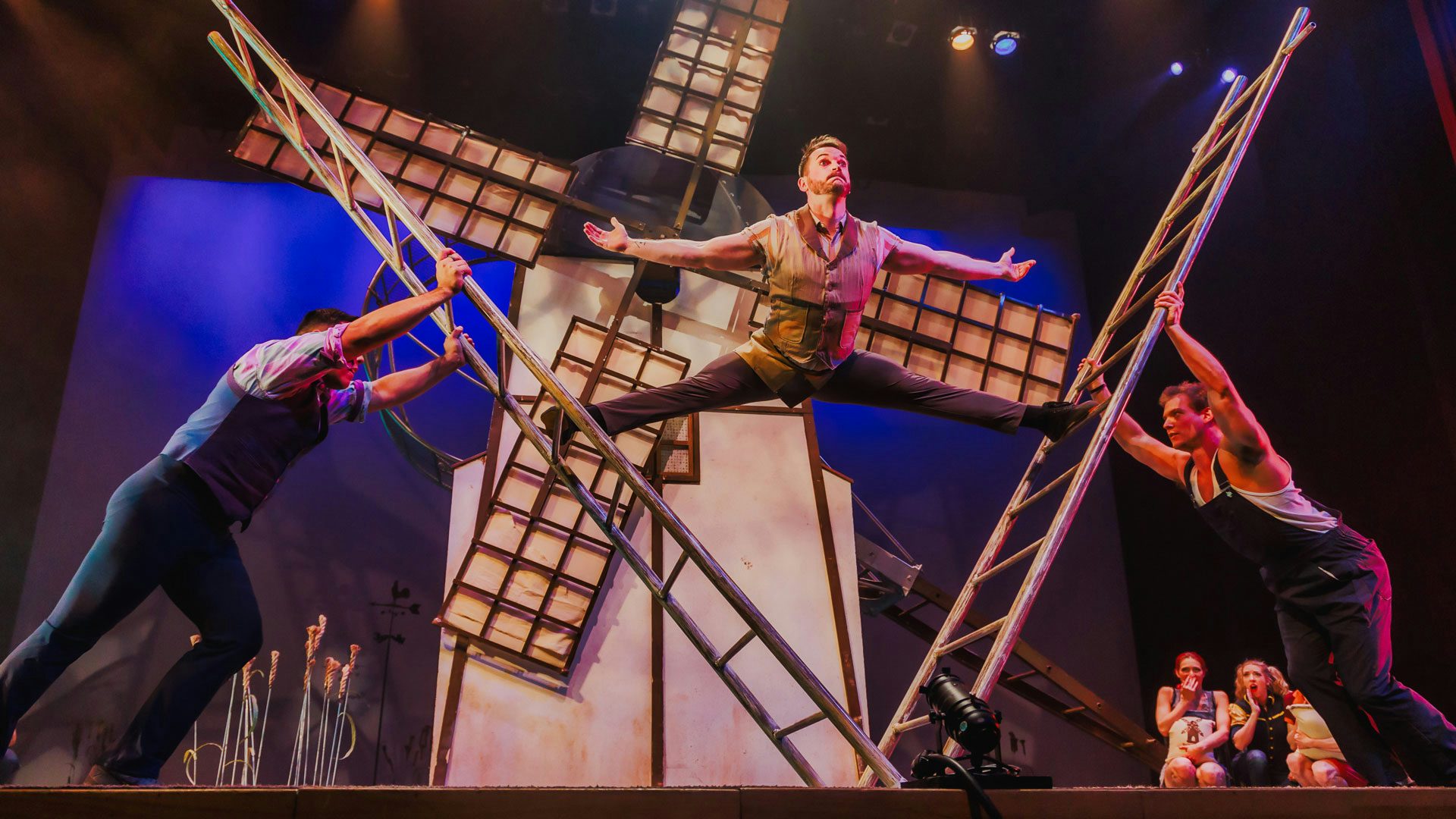 A man balancing himself between two ladders leaning outwards that are being supported by two other men. Two women in the background gasp in astonishment.