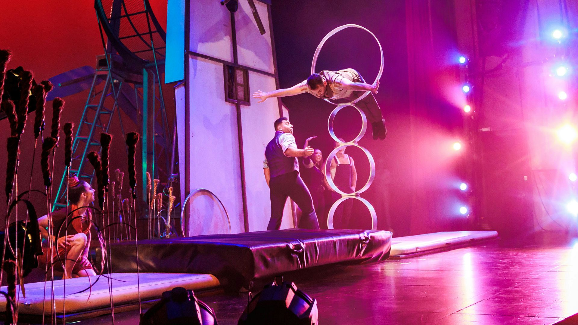 A man jumps through an elevated hoop on stage.