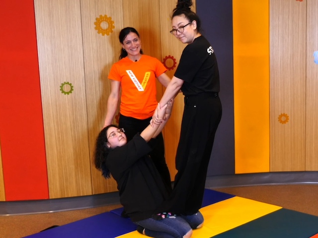 Mana and Keyleen perform a kneeling thigh stand while Gyana spots
