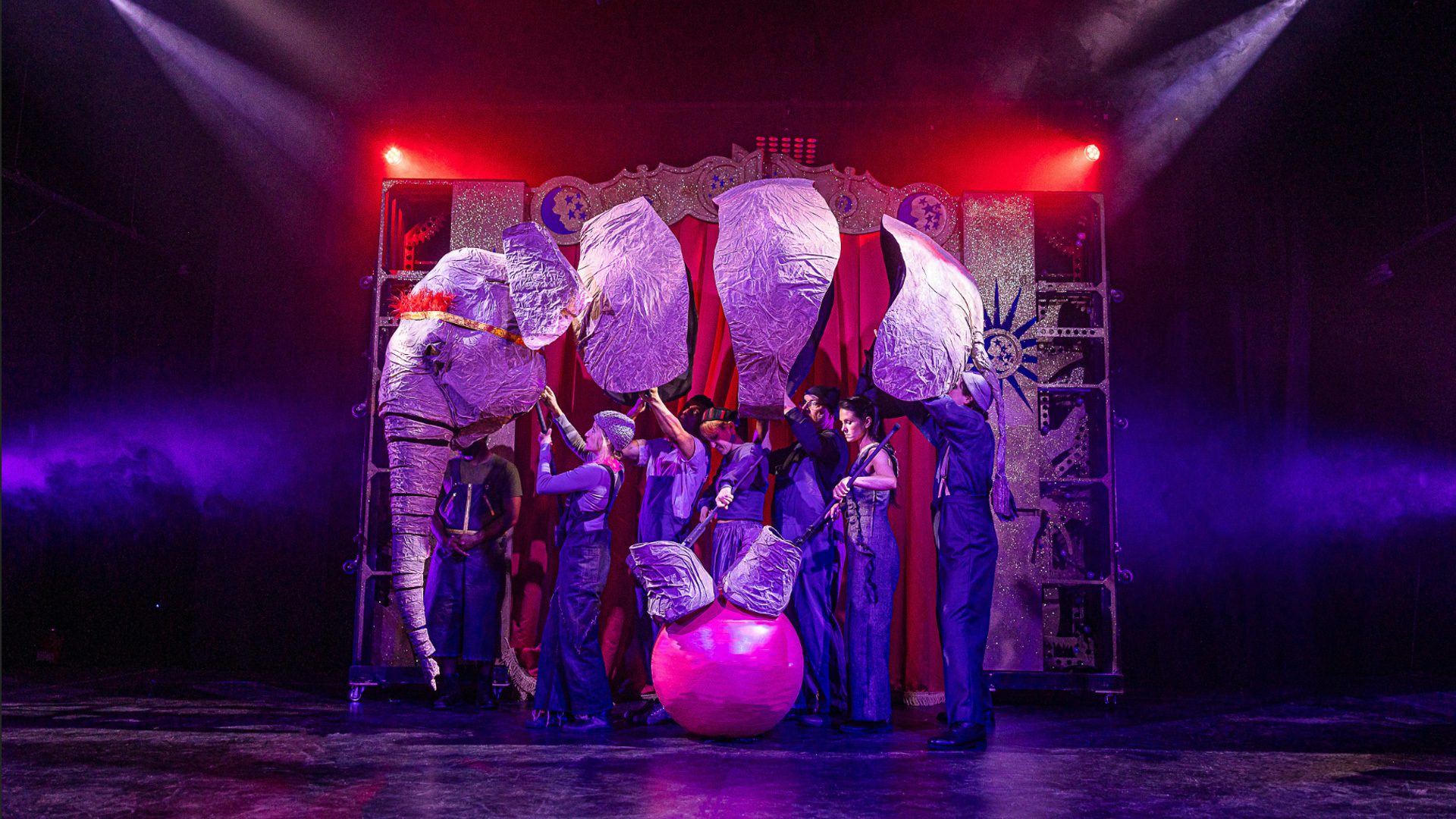 Side view of large elephant puppet balanced atop a small red ball