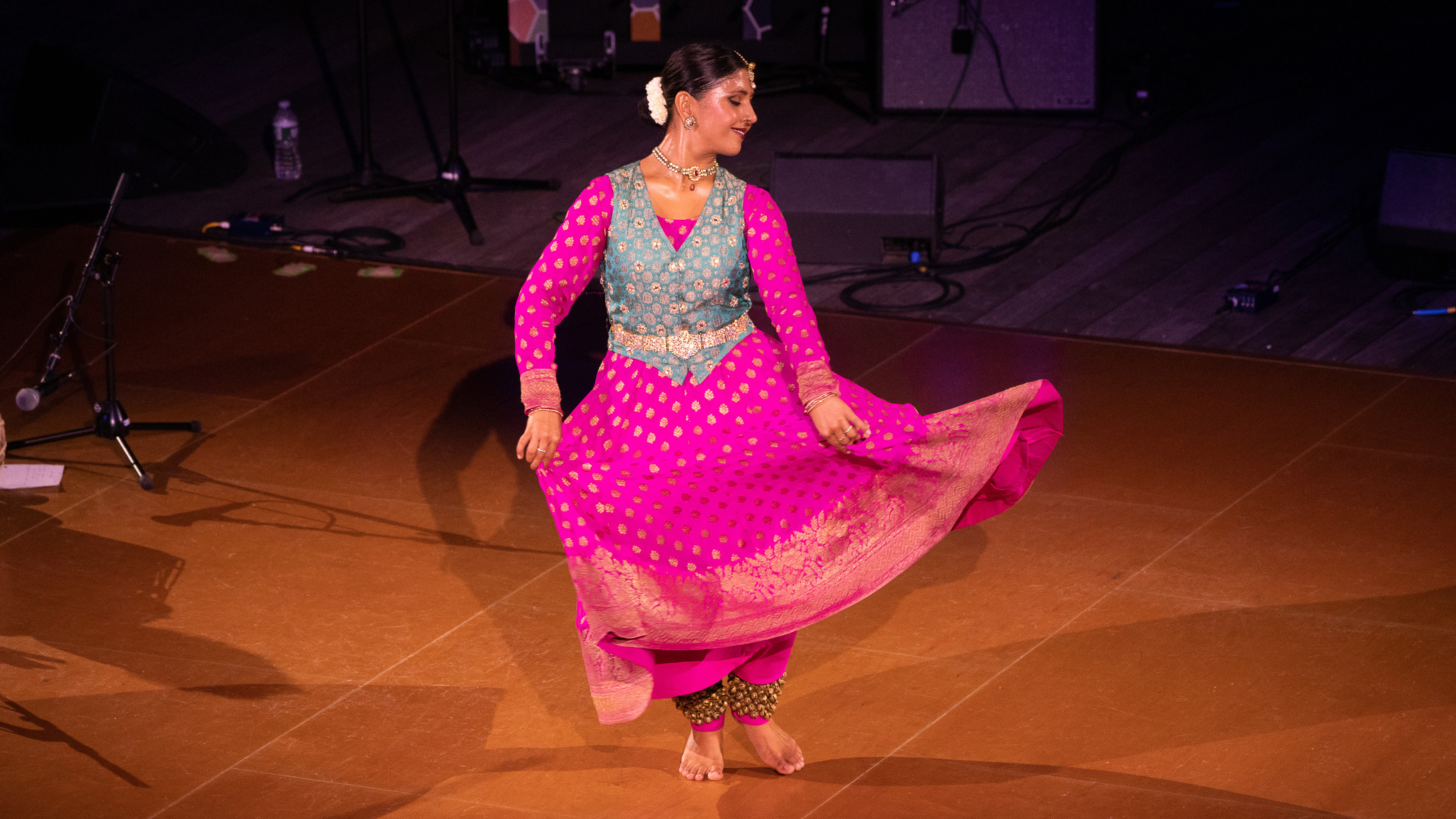 A person wearing a long, pink dress and blue vest looking down and to the right