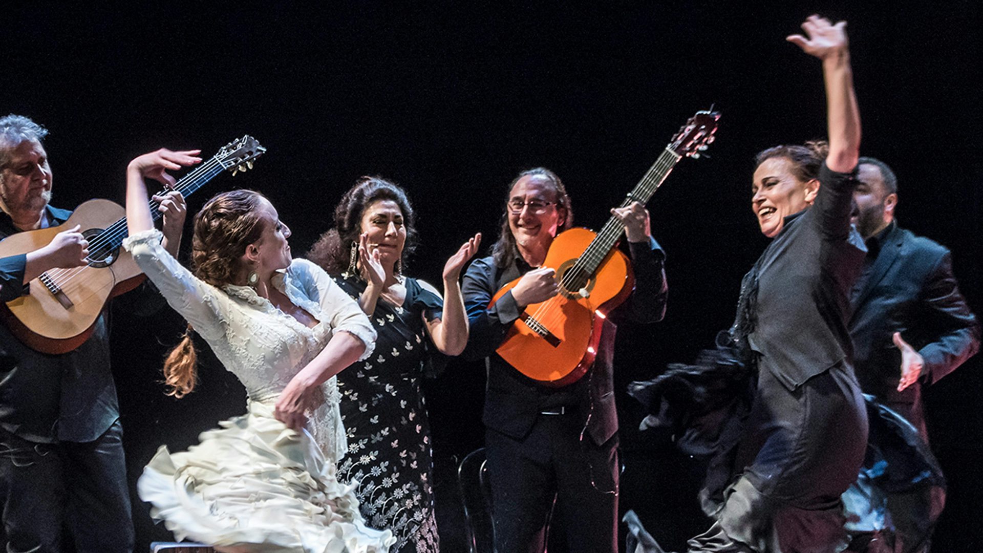 A person in white clothes dancing with a person in black clothes in front of a band of four people