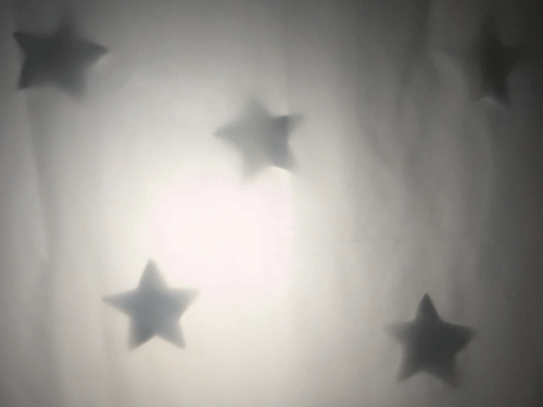 Looping GIF of a moving light behind a sheet with star shapes in shadow
