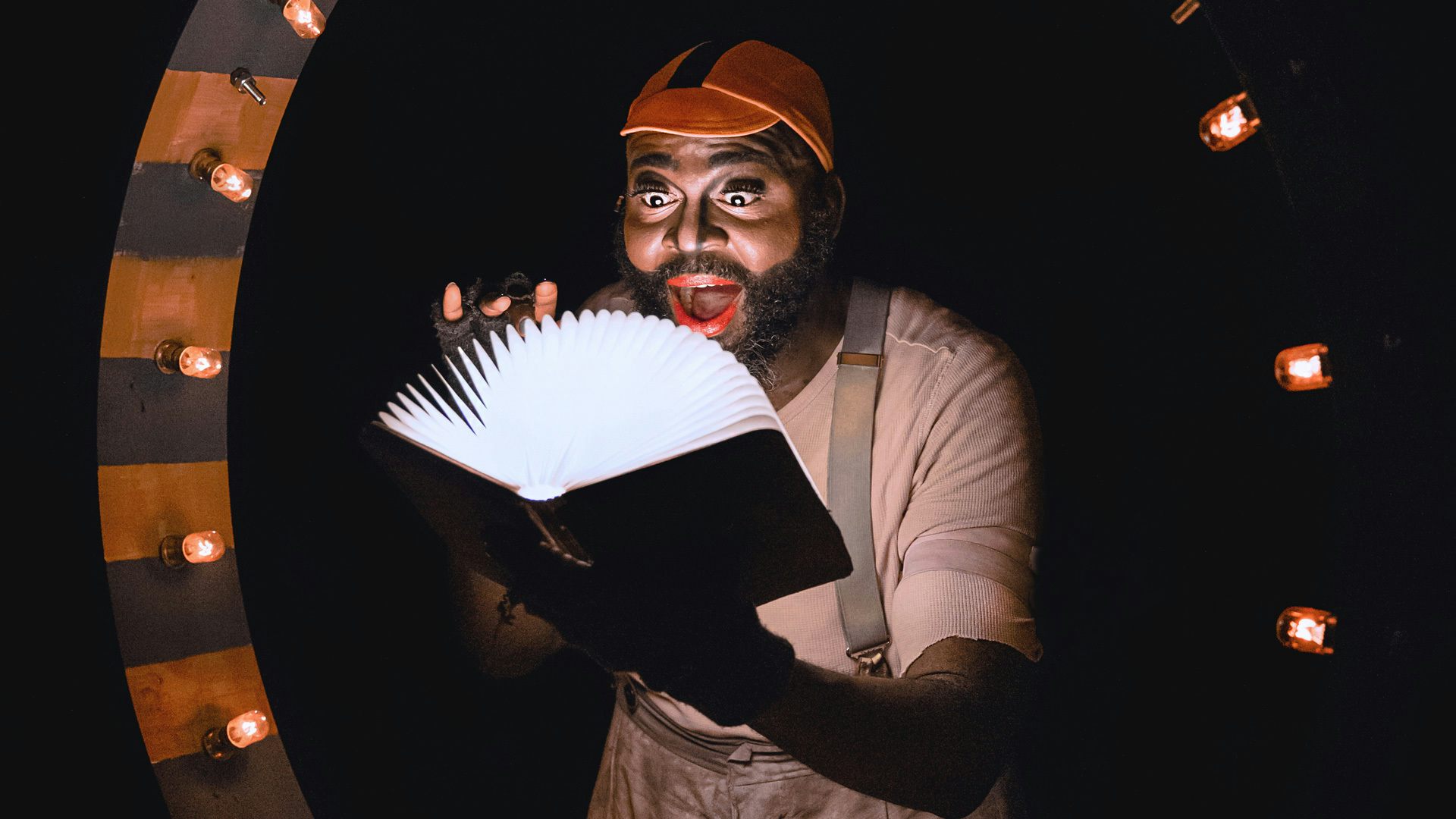A man with a beard holds an open book that has light coming out of it. He has a surprised expression on his face.