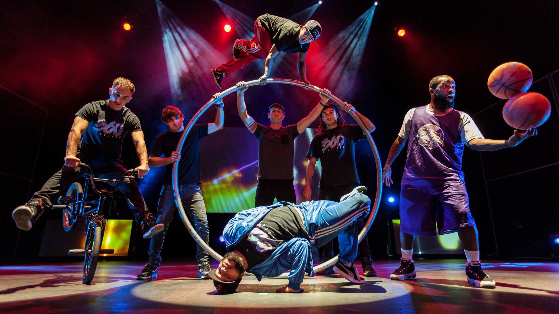 Promotional photo of the cast of 360 ALLSTARS posing on stage: BMX, Cyr wheel, breakdancing, basketball balancing.