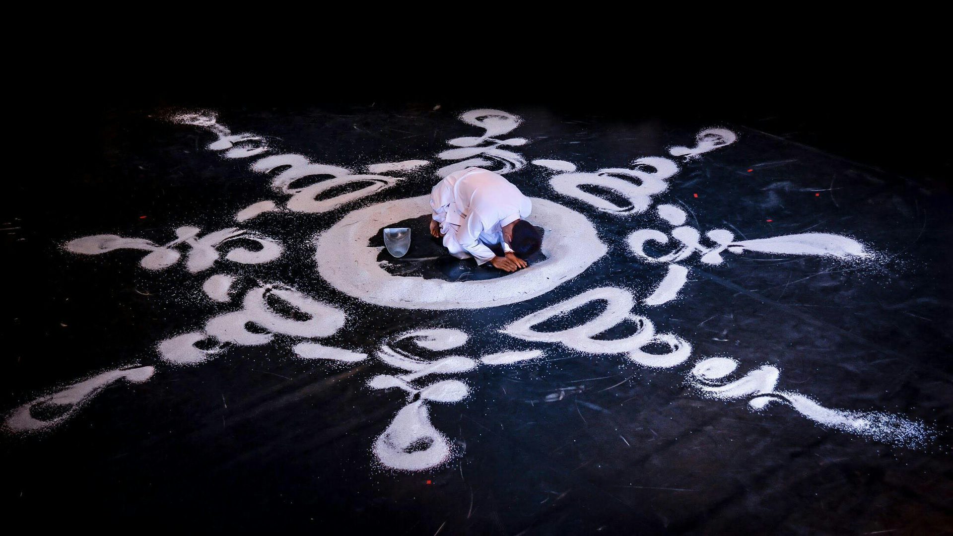 A person draws a large mandala (a Buddhist religious symbol) with white rice around themself.