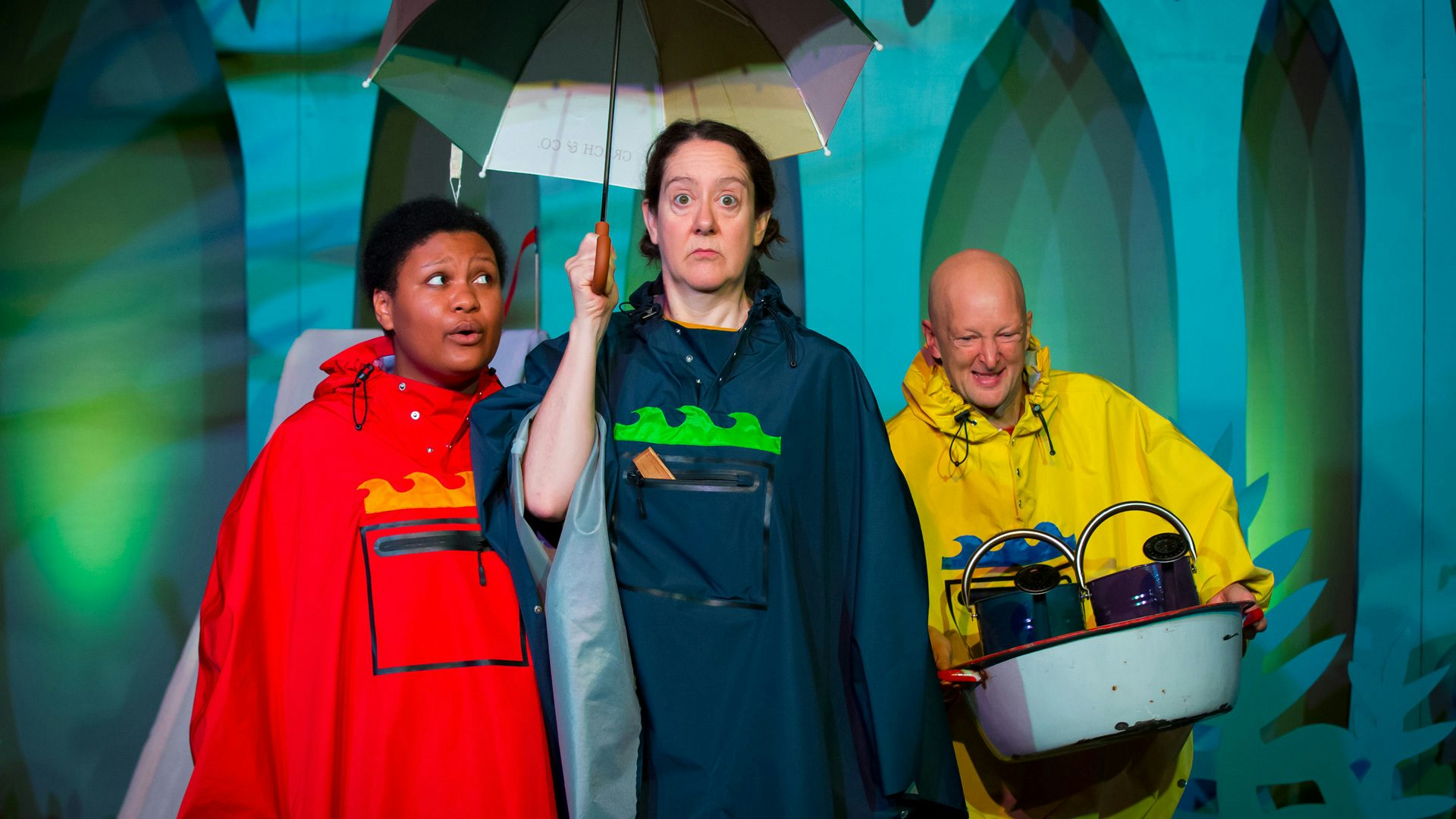 Three people stand next to each other holding a box of gardening supplies and an umbrella. A lime-green light shines behind them.