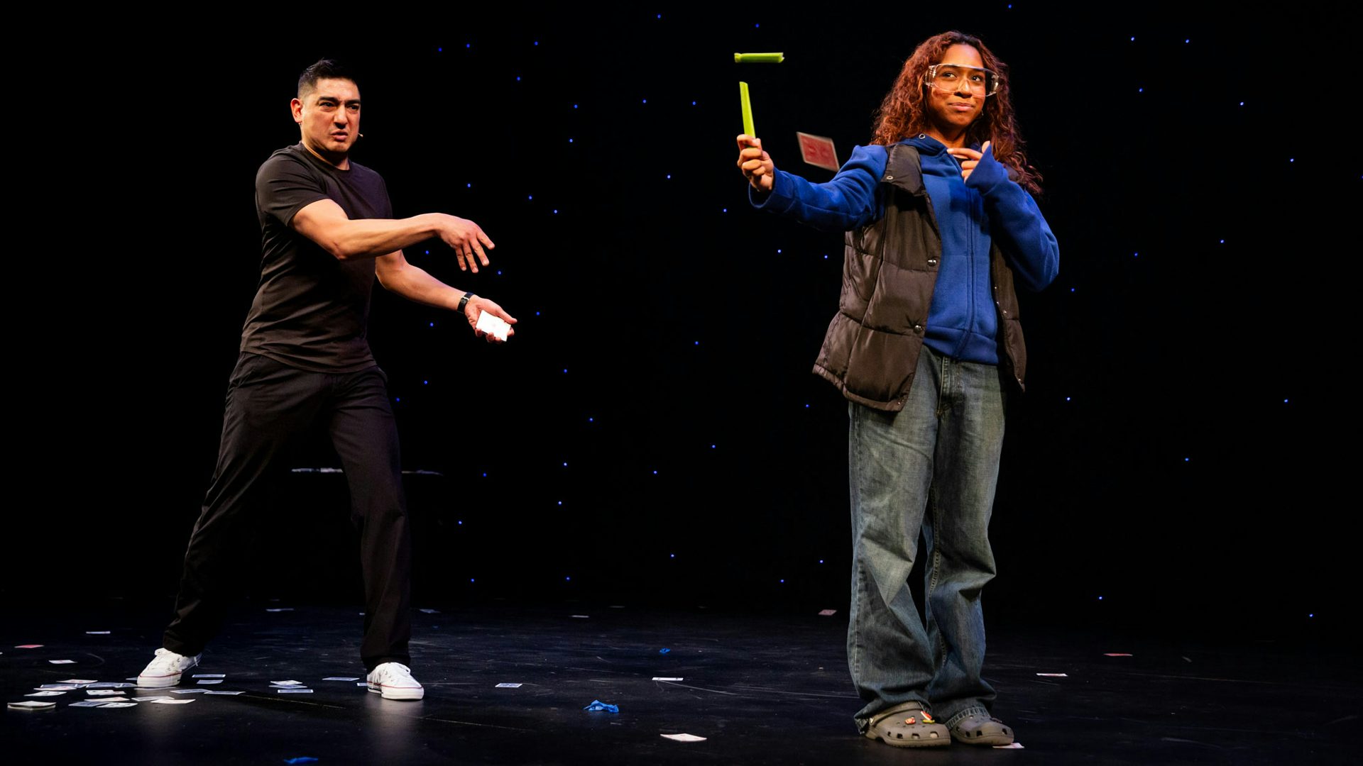 A man in black clothes throws a card at an object held by another person facing away from him