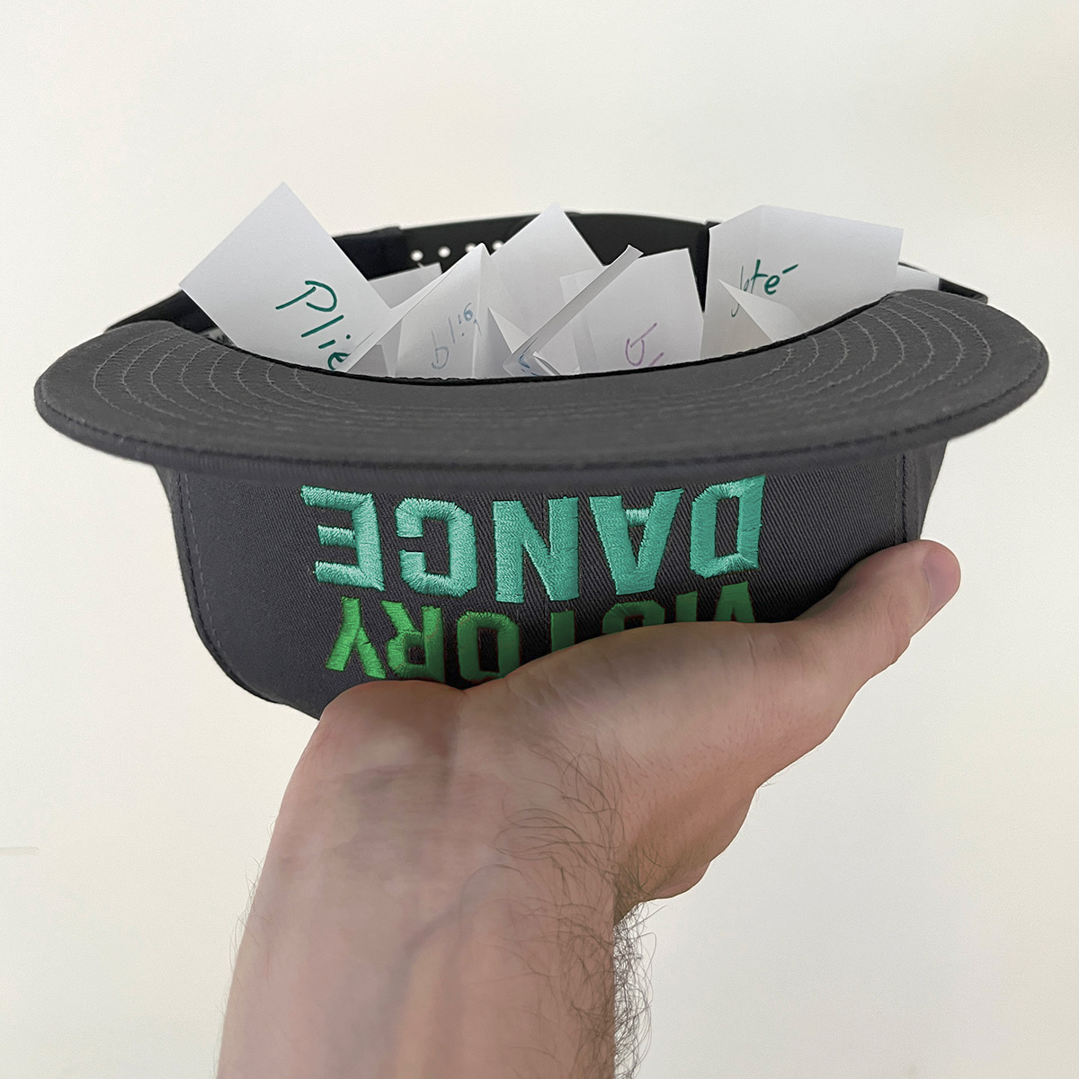 A hand holding a New Victory Dance cap full of folded slips of paper
