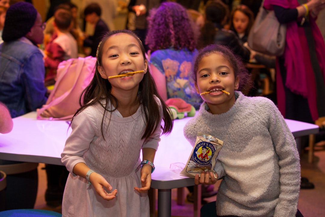 Two young girls with pretzel sticks sticking out of their mouths
