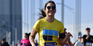 Runner with a brown ponytail and yellow shirt that says New 42 smiles at the camera while running