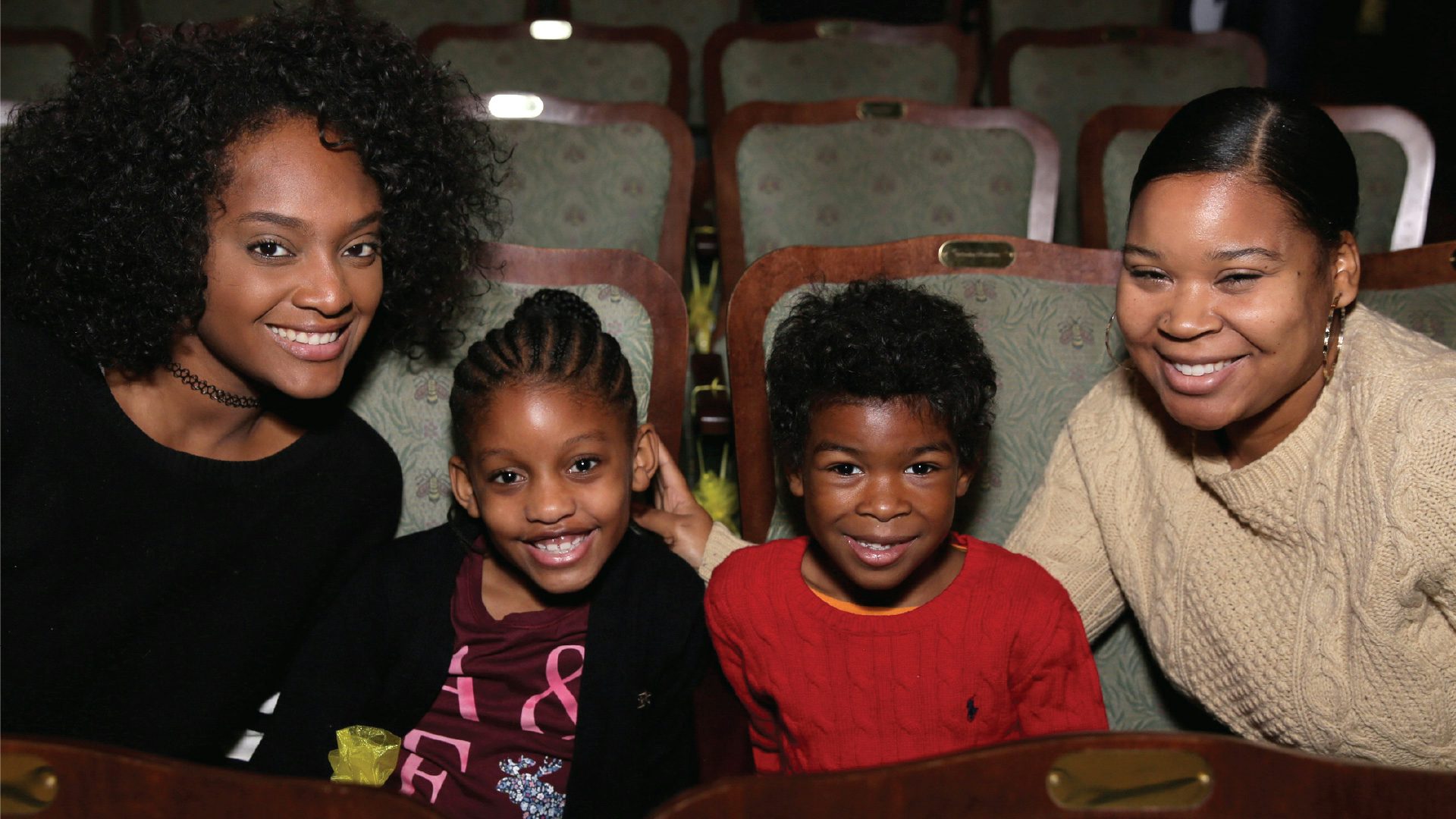 Two women and two kids sitting in theater seats and smiling