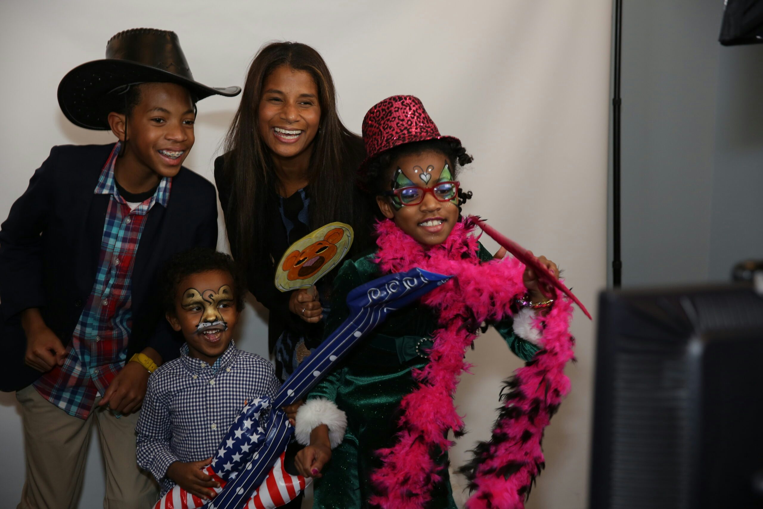 A parent and three kids smile. The kids have face paint, wear costume hats and hold funky props like an inflatable guitar