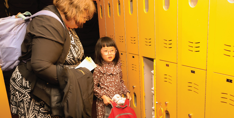 A parent and their child storing their bags in a locker.