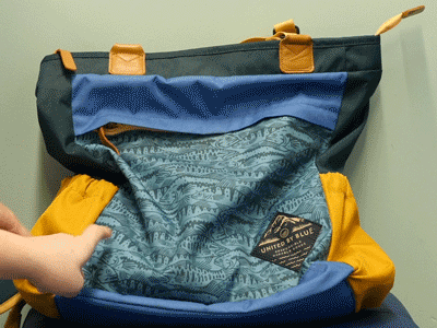 Two sets of fingers run along the perimeter of a teal and yellow patterned backpack.