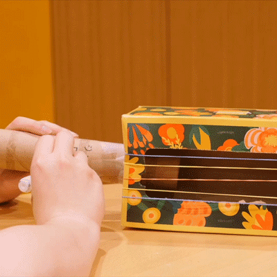 A repeating GIF of the cardboard tube guitar neck being decorated with hand-drawn music notes and a smiley face.