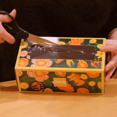 A repeating GIF of scissors cutting away the plastic covering the tissue box's central opening.