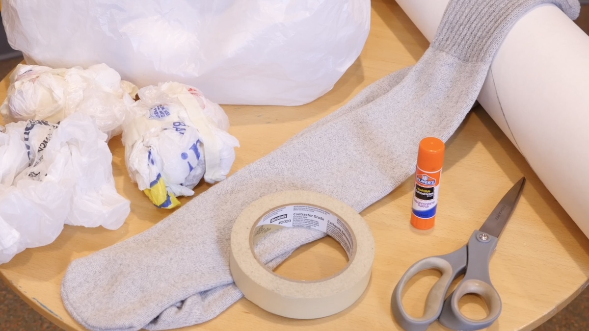 Puppetmaking materials: a tube sock, some masking tape and plastic bags, glue, scissors and a roll of paper