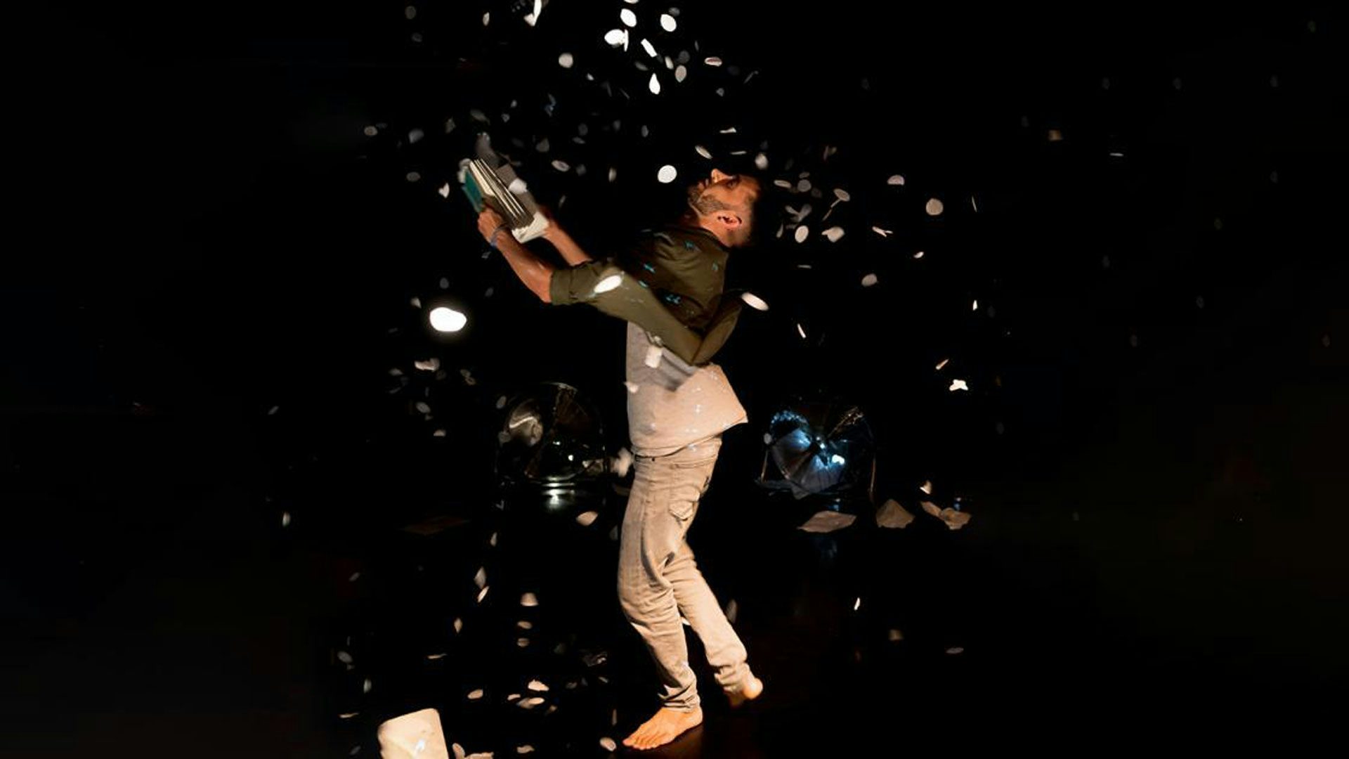 A performer faces to the side and looks up. They hold open a book and glitter flies all around.