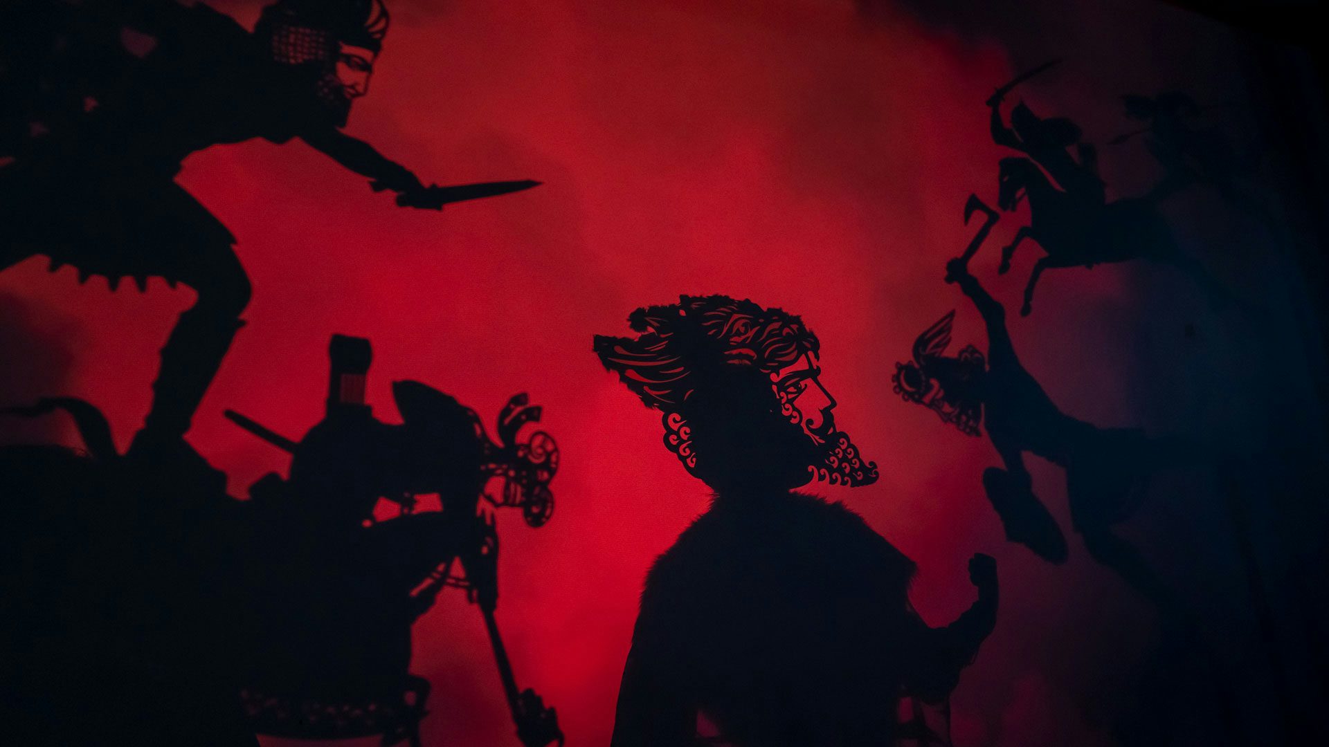 Many shadows of soldiers fight with weapons and on horseback against a deep red backdrop.