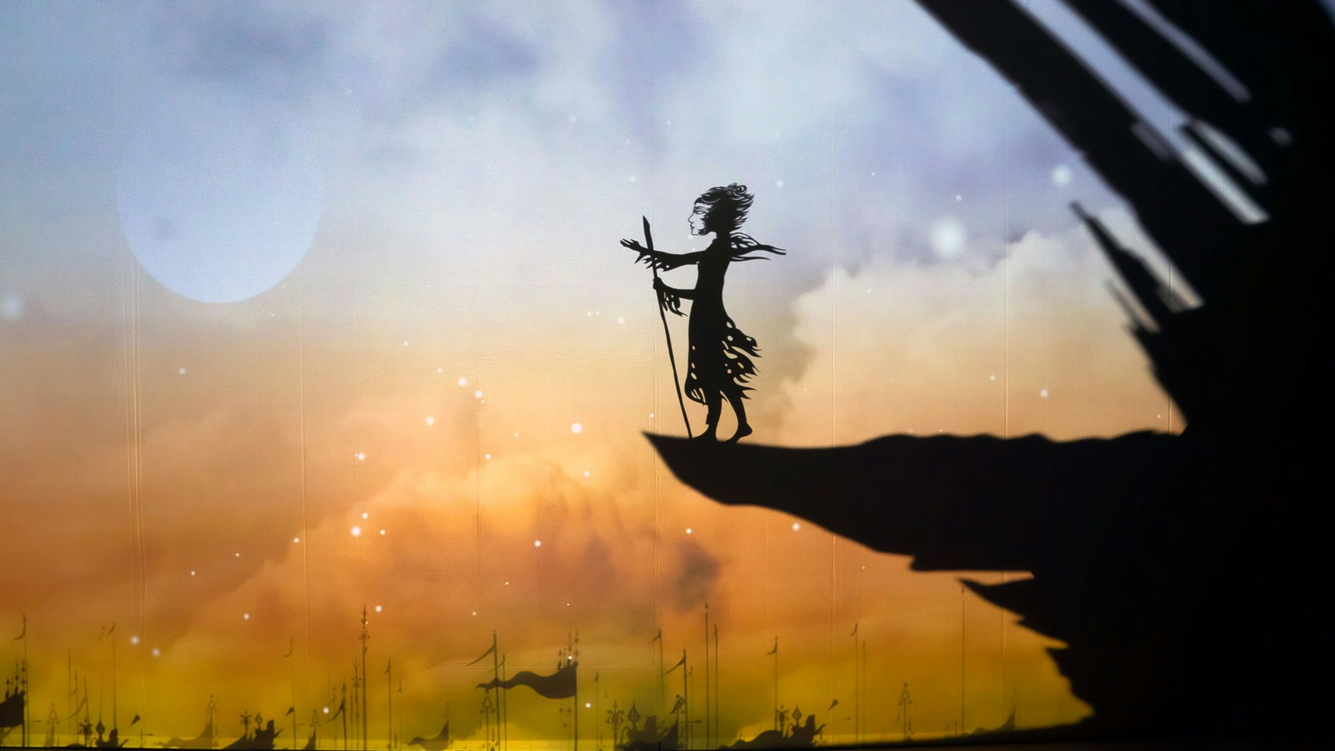 A shadow puppet holding a walking stick stands on a large shadow of a cliff overlooking shadows of soldiers and flags.