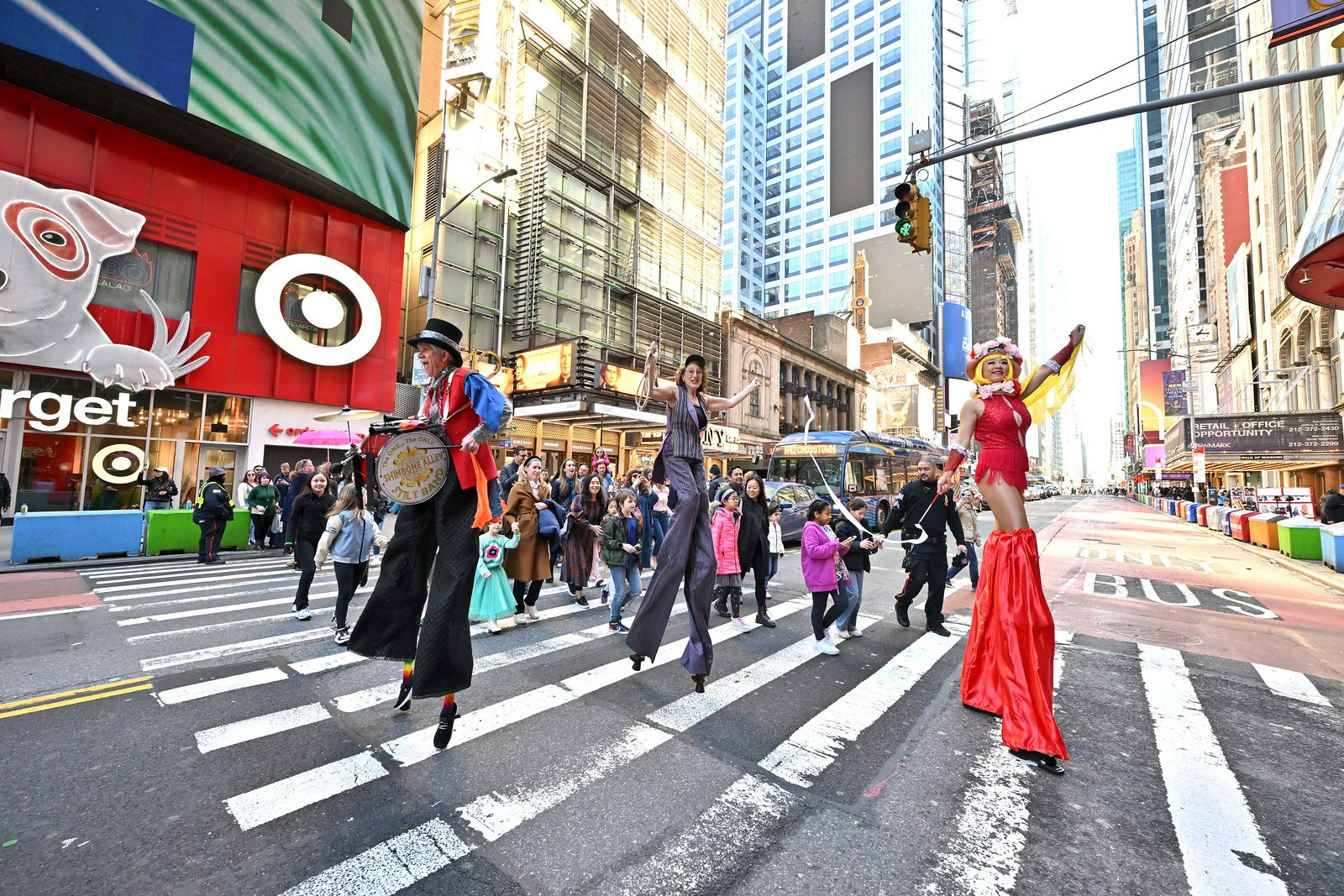 A view of the circus parade across the street led by three performers on stilts.