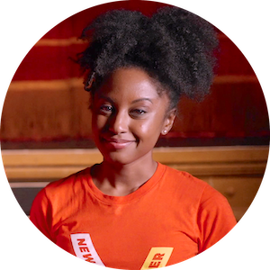 Headshot of Melle Phillips wearing an orange t-shirt with the New Victory Theater logo