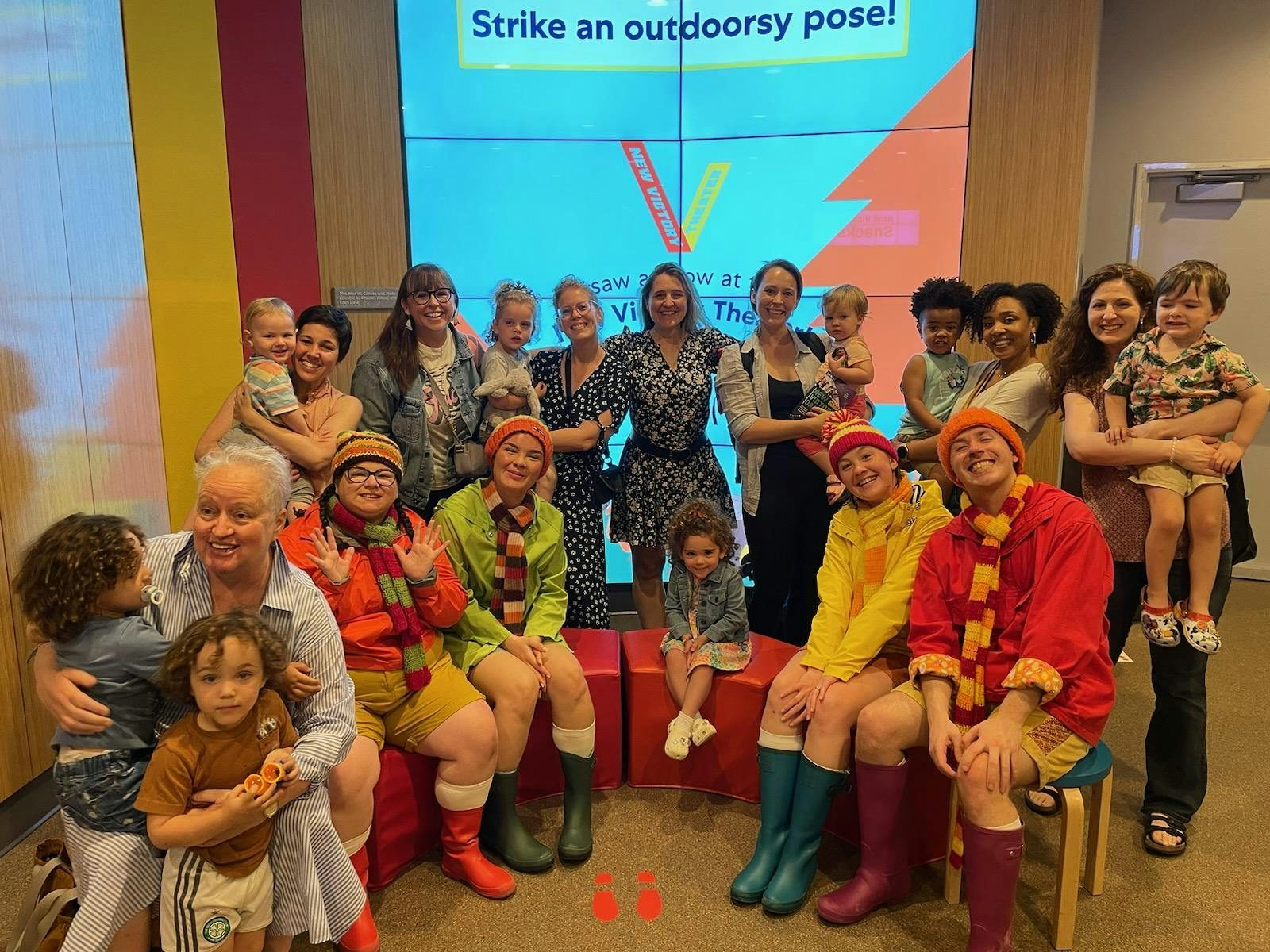 Large group of adults and kids seated with four dancers in beanie hat and wellie boot costumes