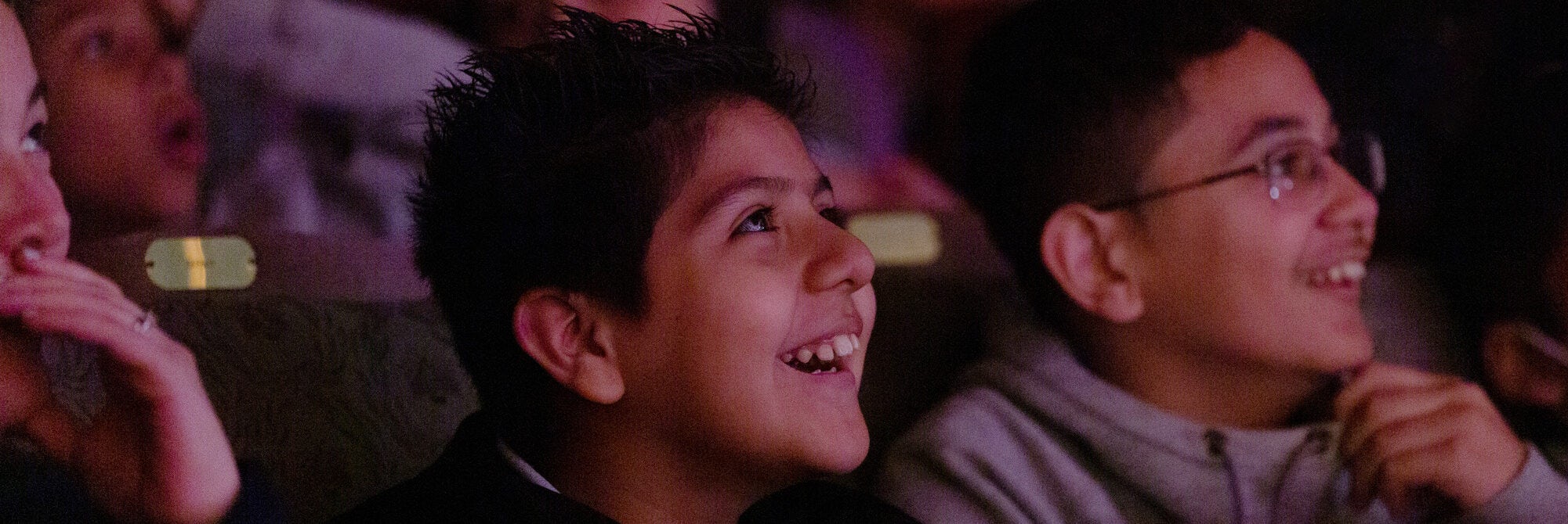 Kids from the audience smiling looking at a performance.