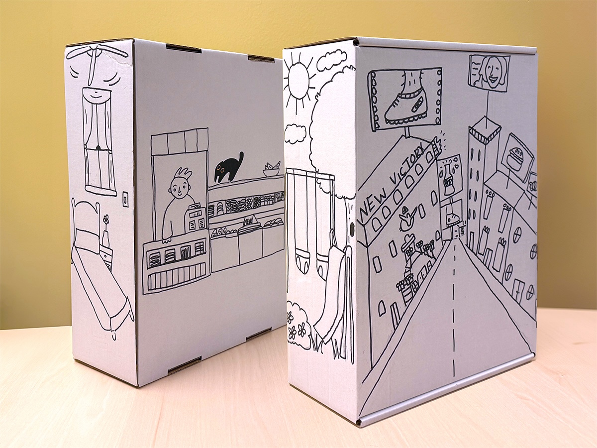 The four sides of Siobhan's shoebox with black marker illustrations of her bedroom, a bodega with a black cat, a playground with swings and a slide, and Times Square with the New Victory Theater visible on one side.